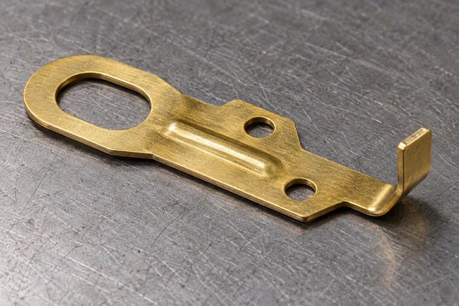 Thin yellow brass sheet-metal electrical terminal tab with an oval eyelet hole, two offset pierced mounting holes, a shallow stiffening bead and one short bent connection tongue; consistent thin sheet wall, no solid machined block — illustrative generated component concept