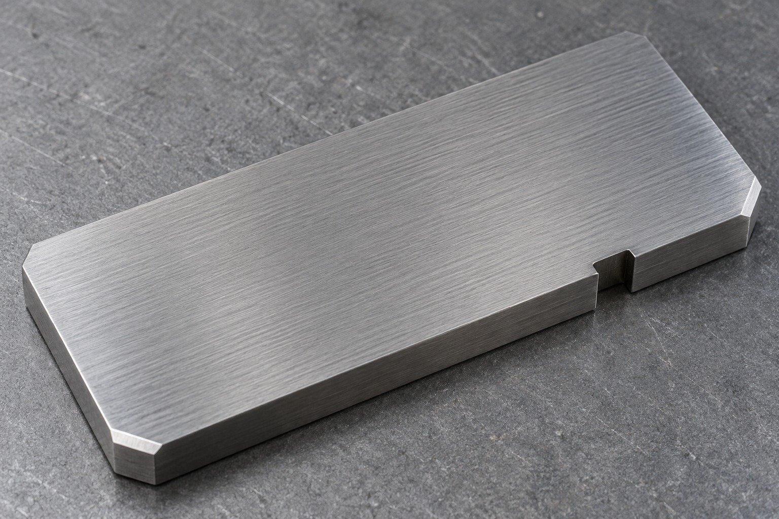 An O1 ground reference coupon with two small chamfers and one offset locating notch, fine uniform parallel grinding texture, neutral steel appearance filling frame — illustrative component concept